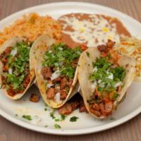 Tacos Al Pastor · Marinated pork loin grilled with fresh cilantro, onions, and spicy tomatillo sauce on the si...