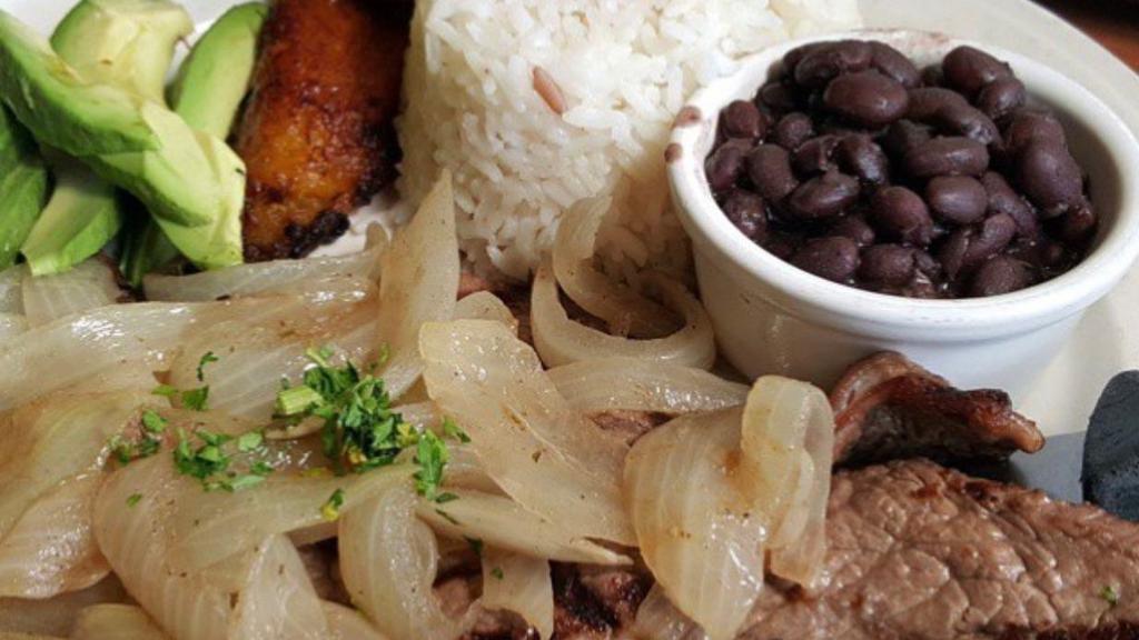Palomilla · Gluten-free. Thin cutlet of choice top round seasoned and quickly grilled. Topped with grilled onions. Served with white rice, black beans and sweet plantains.