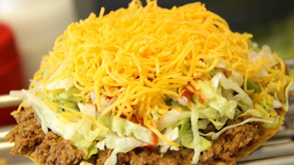 Beef Tostada · A flat, crisp corn tortilla covered with taco meat, then topped with lettuce, a squirt of hot sauce (of course) and freshly grated Colby cheese. Gluten-Free.
