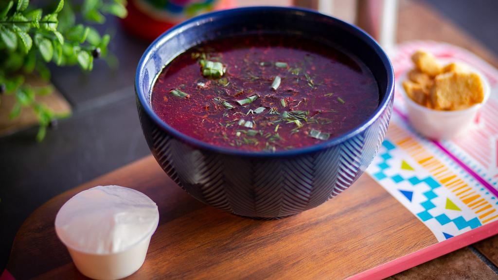 Borscht · Delicious Ukrainian borscht soup made with fresh red beets, grass fed beef, onions, carrots, potatoes, served with the spoon of sour cream and fresh herbs.