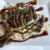 Carne Con Crema De Maiz · Marinated skirt steak on a bed of creamed corn drizzled with chipotle bourbon sauce.