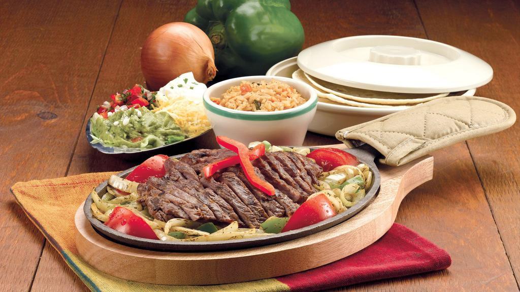 Steak Fajitas · Flame grilled and rushed to your table in a sizzling skillet with lightly seasoned caramelized onions, tomatoes and fresh poblano and red peppers. Served with sides of guacamole, pico de gallo, our Jack and Cheddar cheese blend and sour cream topping. Includes warm flour tortillas and Spanish rice.