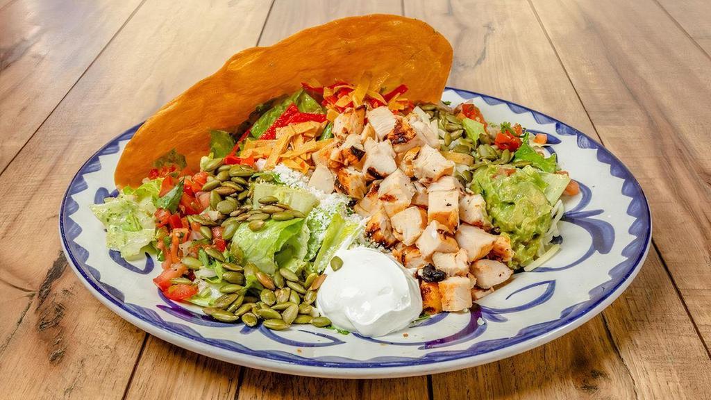 Grilled Chicken Taco Salad · Homemade tostada taco shell filled with romaine lettuce, refried beans, pico de gallo, cotija cheese and jack cheese. Topped with grilled chicken, roasted pepitas, sour cream, guacamole and your choice of dressing.