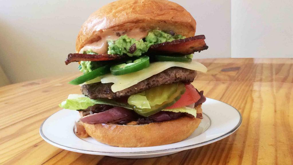 The Oaxaca Burger · A towering burger with cheddar, bacon, guacamole, jalapenos, caramelized onions-black pepper mayo with tomato, pickles, romaine, and grilled onions served on a perfect brioche bun.