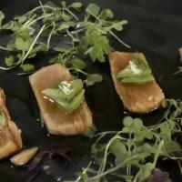 Salmon Carpaccio · Sesame marinated salmon sashimi topped with avocado cream sauce and herbs.