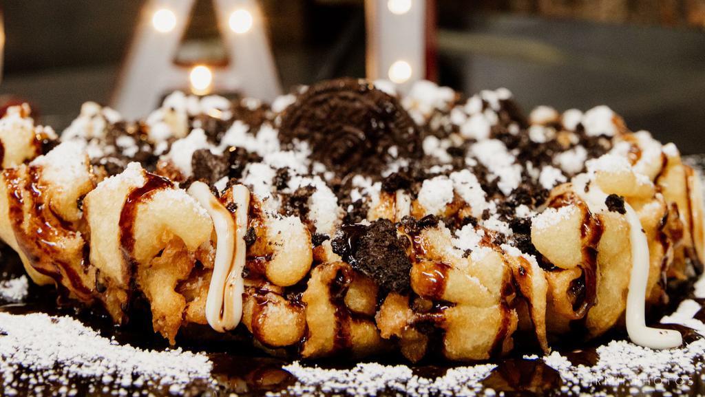 Oreo Cookie Funnel Cake · Freshly prepared funnel cake, sprinkled with powdered sugar, cream cheese drizzle, crumbled Oreo cookies, topped with chocolate drizzle and whole Oreo cookies.