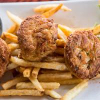 Crab Cakes · Three crab cakes over a bed of old bay fries with coleslaw and tarter sauce.