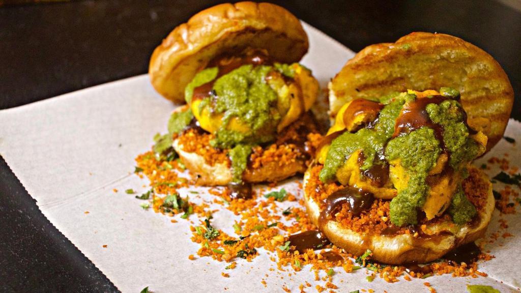 Vada Paav · Crispy batter-fried mash potato fritter, topped with spicy garlic & tangy cilantro-mint chutneys, served on a toasty buttered roll. Served with potato crisps.
