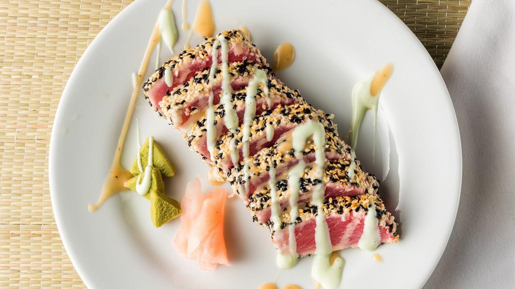 Sesame Crusted Tuna · Saku Ahi tuna, crusted in tuxedo sesame seeds, lightly seared, sliced and topped with cucumber wasabi and sesame ginger sauces. Served with fresh seaweed salad, pickled ginger, and wasabi.