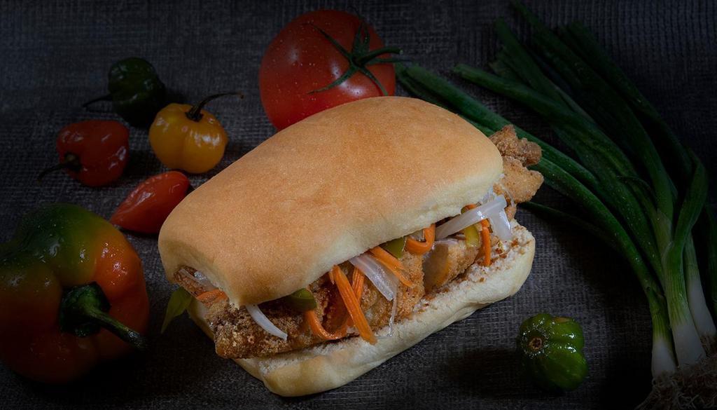 Escovitched Fish Sandwich · Hand-breaded red snapper filet marinated in our signature escoveitch sauce of vinegar, onions, peppers, and allspice, then lightly fried and served inside coco bread with a scotch bonnet pepper aioli.