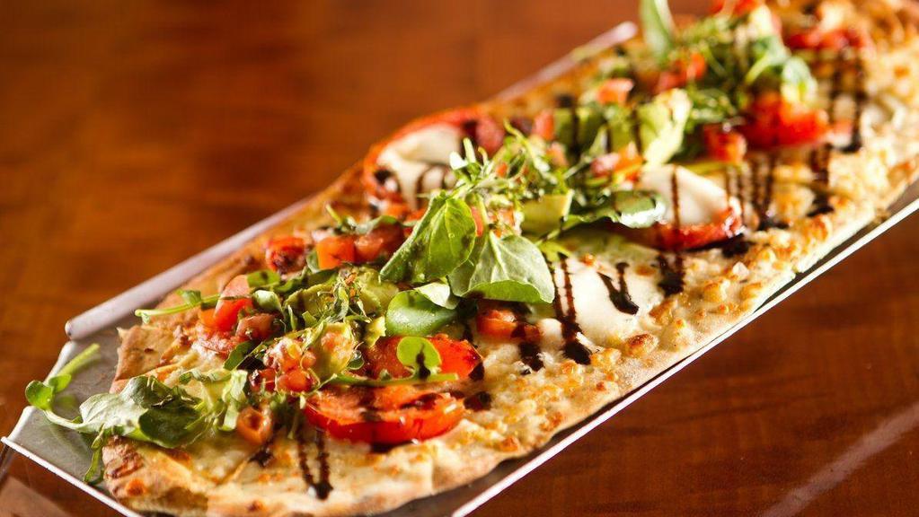 Caprese Flatbread · brushed with extra virgin olive oil & fresh herbs, layered with oven roasted tomatoes, parmesan, fresh mozzarella, topped with a mix of basil, arugula, fresh tomatoes, & avocado tossed in olive oil & sea salt