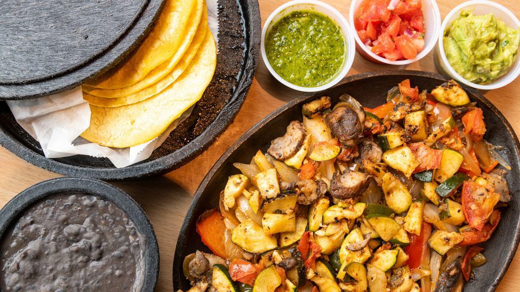 Vegan Fajitas · mushrooms and zucchini served over peppers & onions with guacamole,.  salsa verde, pico, black beans, corn tortillas