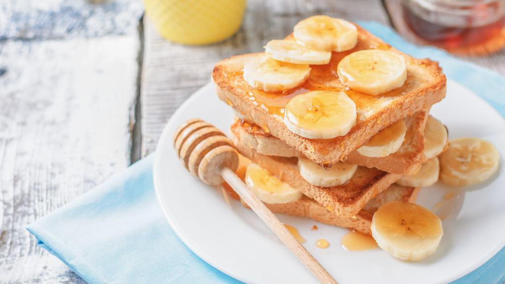 Banana French Toast · Sliced challah bread soaked in eggs and milk, then fried and topped with bananas, served with a side of butter  and syrup.