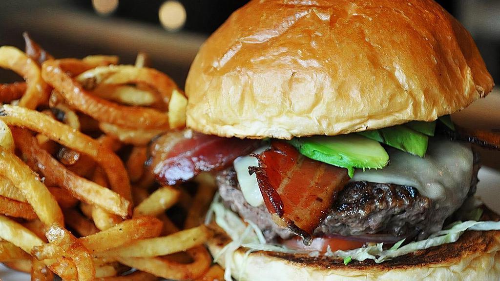 Avocado Bacon Burger · Topped with white cheddar, smoked bacon, sliced avocado, lettuce, tomato, onion, bread & butter pickles, and our zesty Louie sauce (a combo of mayo, tomato, relish, lemon, and spices). Served on our brioche bun..