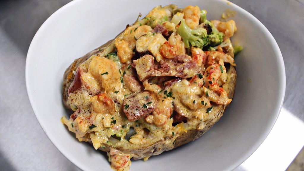 Fully Loaded Cajun Baked Potato · Russet potato overstuffed with sausage, shrimp, crawfish tails, chicken, and broccoli, topped with secret spicy cheese sauce, green onions and shredded cheese