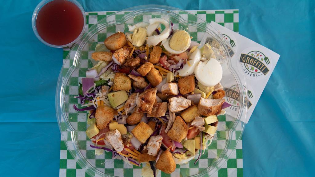 Cobb Salad · Fresh crisp romaine lettuce, sliced tomatoes, sliced boiled
eggs, chopped bacon, red cabbage, shredded Cheddar and mozzarella cheese, sliced avocado, red onion, croutons, grilled marinated chicken, kosher salt, ground black pepper, red wine vinaigrette dressing. Variation: comes with one protein.