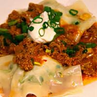 Aushak · Ravioli filled with scallions, served with mint garlic yogurt sauce and topped with ground b...