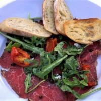 Beef Carpaccio · Horseradish crema, truffle oil, baby arugula, oven-dried tomatoes, fried capers, baguette