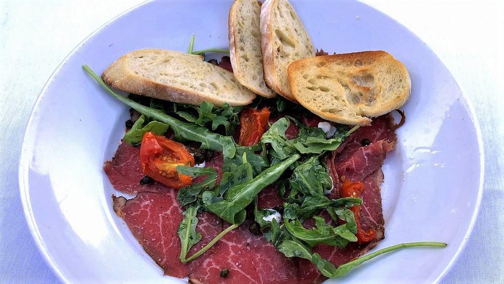 Beef Carpaccio · Horseradish crema, truffle oil, baby arugula, oven-dried tomatoes, fried capers, baguette