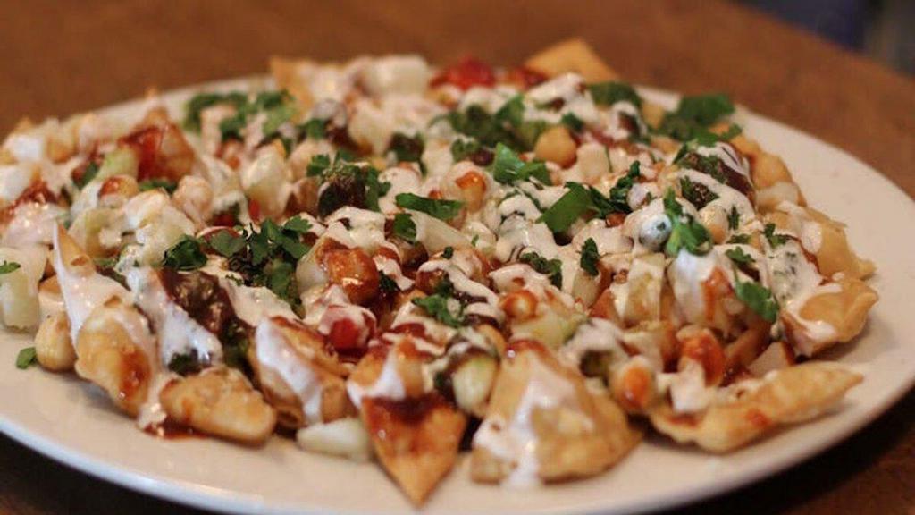 Aloo Chat Papri · Puffed potatoes mixed with chickpea, tomato, and onions, topped with yogurt, mint, and tamarind sauce.