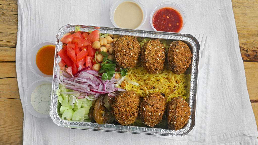 Falafel Over Rice · Falafel with basmati rice, side salad, garbanzo chickpeas, pickles, red onion, lime slice, tahini, tzatziki sauce, and hot sauce.