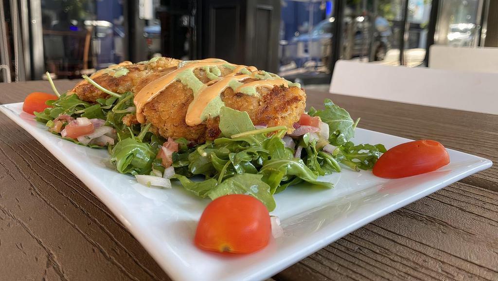 In-House Crab Cakes · Lumps of crab meat and vegetables lightly breaded and pan seared, drizzled with cilantro chipotle crema sauce. Served over baby arugula and chunky mango salsa.