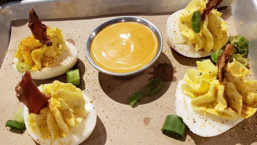 Deviled Eggs · Four deviled eggs topped with candied bacon and served with a side of paprika aioli dipping sauce.