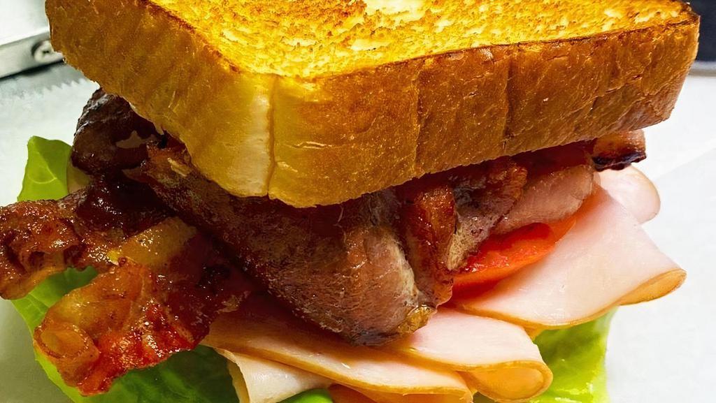 Turkey Club Sandwich · Sliced smoked turkey with garlic aioli, lettuce, tomato, cheddar cheese, and crispy bacon on a fresh bun.