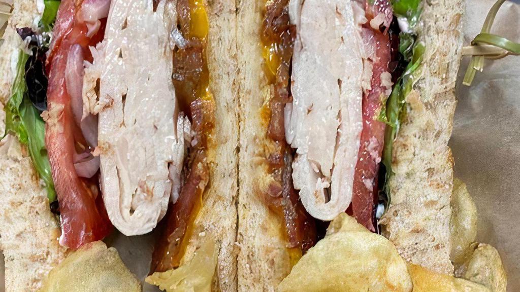Turkey Club Sandwich · Turkey, crisp applewood bacon, Cheddar cheese, tomato, red onion, mayonnaise, dijon mustard, baby greens, and your choice of toasted bread. Served with chips.