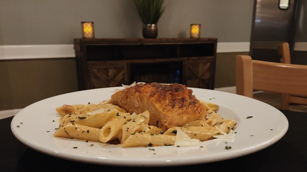Blackened Salmon Alfredo · Blackened salmon served over a bed of penne pasta, tossed in our homemade alfredo sauce. Garnished with shaved Parmesan cheese.