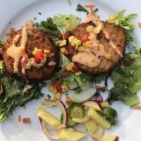 Blue Crab Cakes · Two blue crab cakes topped with sweet roasted corn, chipotle chili sauce on a bed of baby gr...
