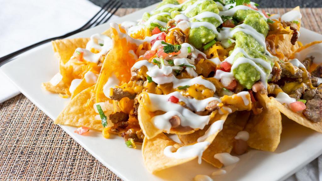 Nachos De Carne Enchilada / Spicy Meat Nachos  · served w/beans, onions, tomatoes, sour cream, cheese, jalapeño, and guacamole.