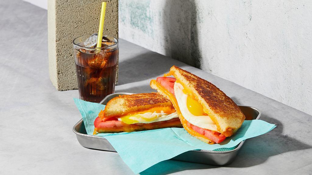 The Breakfast · Melted Cheddar cheese with a fried egg and tomato grilled between two slices of buttered bread.