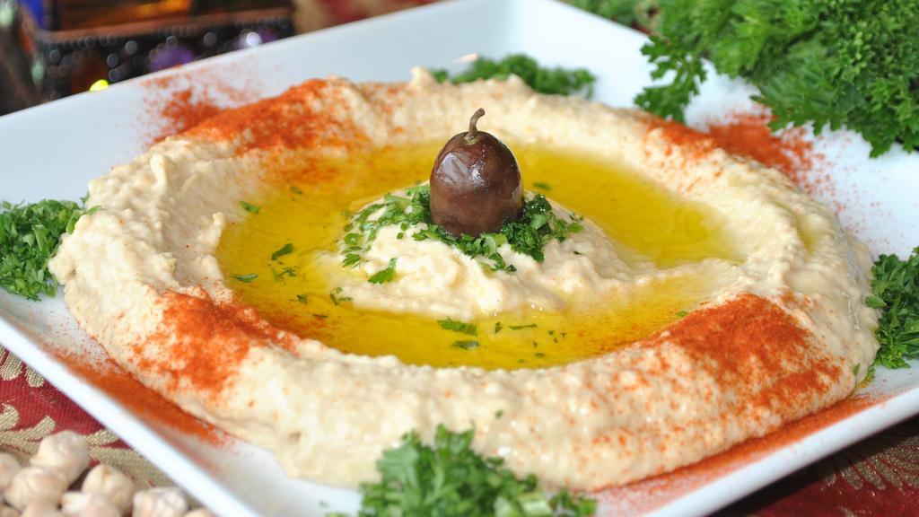 Traditional Hummus · Tasty blend of garbanzo beans, garlic, lemon juice and sesame seed paste topped with olives, paprika, parsley and olive oil. Served with a warm homemade pita bread