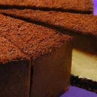 Chocolate Ganache Cheesecake · New York style cheesecake topped with a thick, rich layer of chocolate ganache, sits on a ch...
