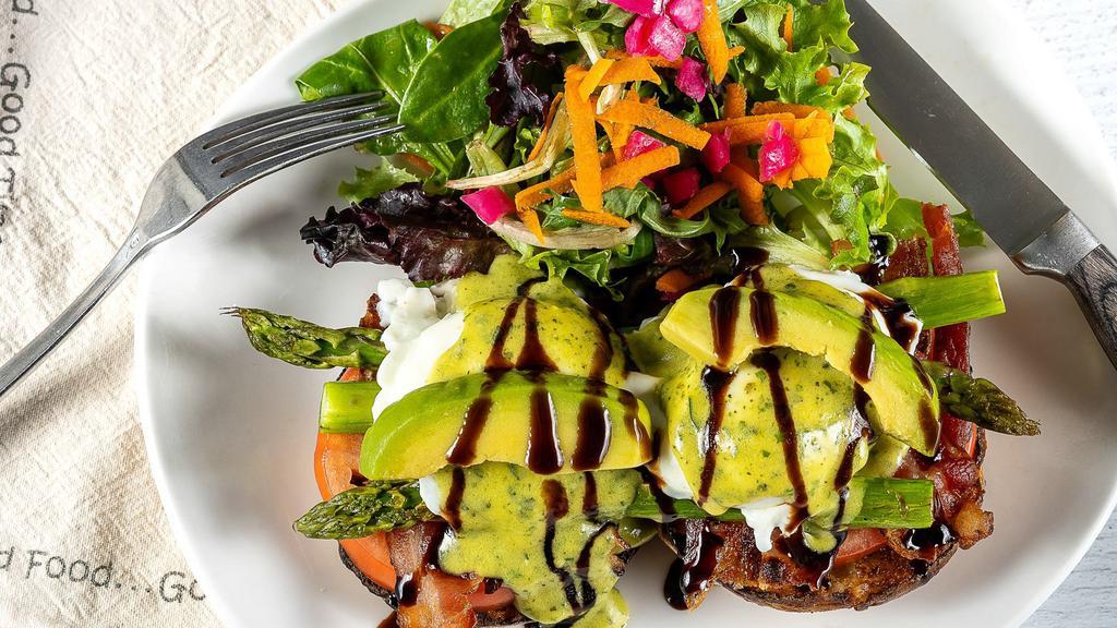 Asparagus Avocado Bacon Benedict · Two perfectly poached eggs layered w/grilled asparagus, vine-ripened tomato, hickory-smoked bacon + sliced avocado w/pesto hollandaise + a balsamic drizzle, over a toasted English muffin + served w/crispy home fries.