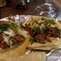 Tacos De Carnitas · Roasted marinated pork on top of corn tortillas garnished with chopped onion and cilantro.