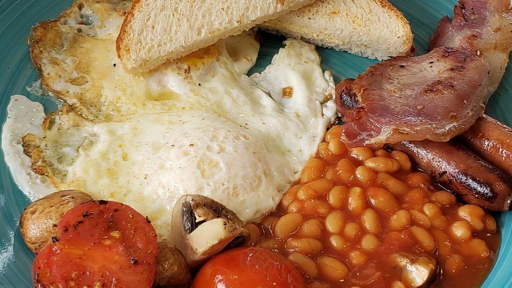 English · Two eggs sunny side up, one banger sausage link, slice of Irish bacon, tomato beans, fried tomatoes, mushrooms and toast.