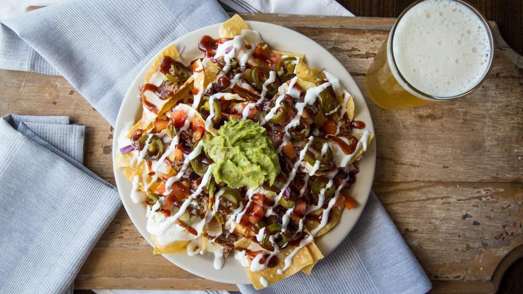 Burnt-End Nachos · House-made queso, jalapeños, sour cream, guacamole, tomato, red onion, KC burnt ends and BBQ sauce.