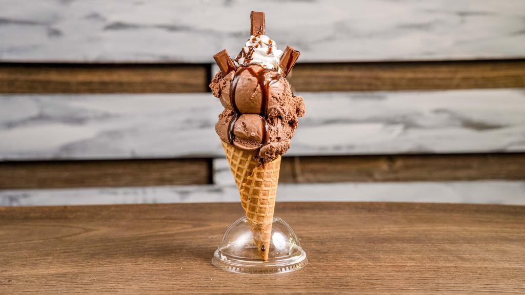 Kit Kat Krumble · Chocolate ice cream in a waffle cone drizzled with chocolate syrup and topped off with whip cream and kit kats.