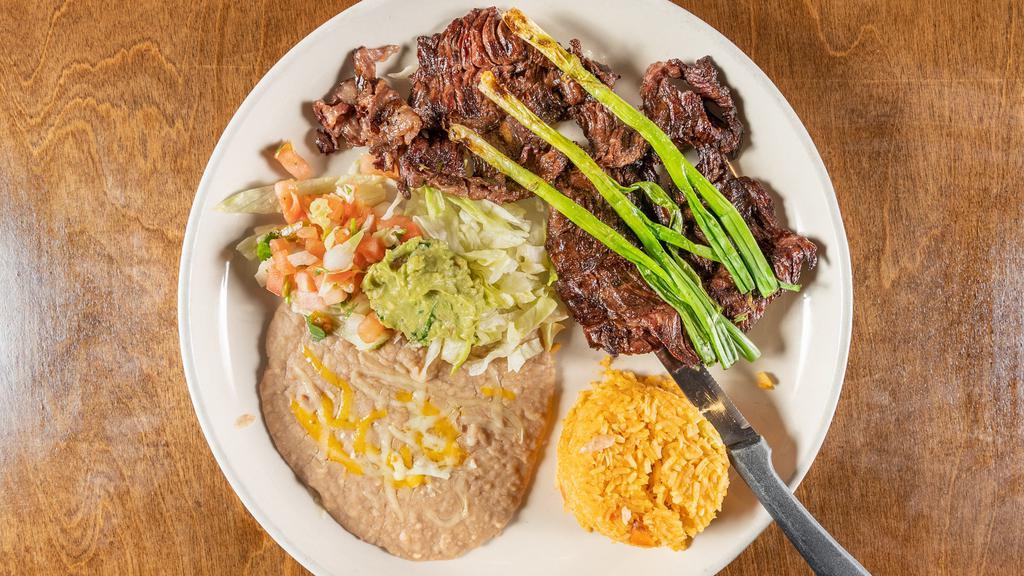 Carne Asada · Thin slices of skirt steak charbroiled and garnished with green onions and guacamole. Served with rice and beans.