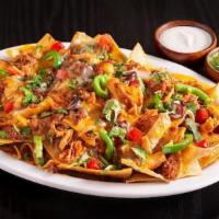 Nachos Magnifico · A plate of corn tortilla chips topped with taco meat, shredded chicken, pinto beans, and you...