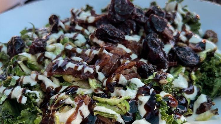 Brussels Sprout And Kale Salad · Gluten-free. Oven-roasted brussels sprouts and kale, crumbled bacon, candied pecans, dried cherries, goat cheese crème, and balsamic reduction. Served warm out of the oven!